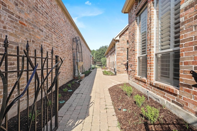 view of side of property featuring a patio, brick siding, and fence