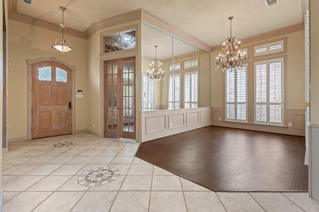 entryway featuring light tile patterned flooring, a decorative wall, a notable chandelier, visible vents, and crown molding