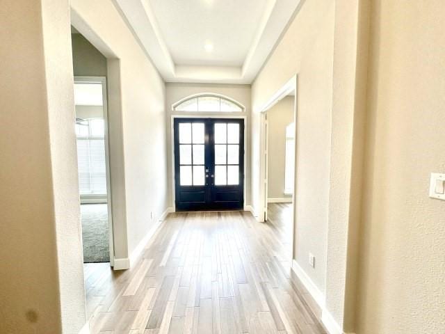 entryway featuring light wood-style flooring, a tray ceiling, baseboards, and french doors