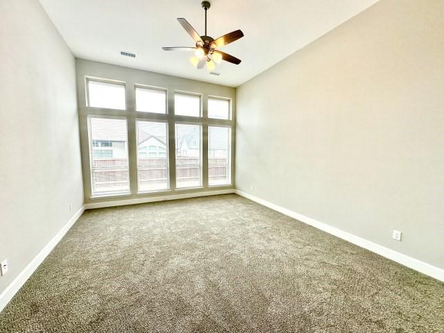 carpeted spare room with visible vents, a ceiling fan, and baseboards