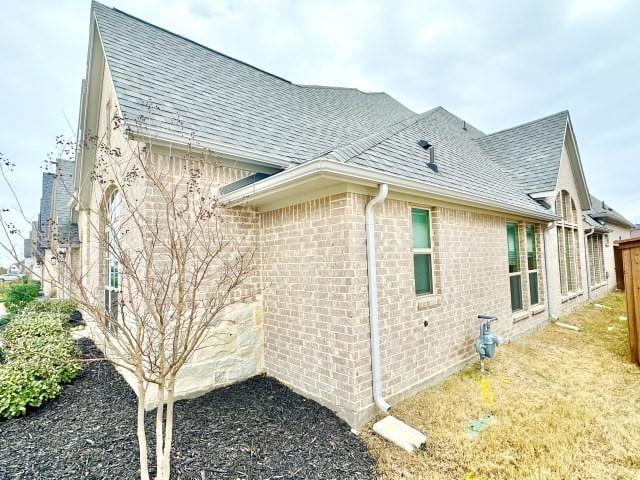 view of side of home with brick siding, roof with shingles, and fence