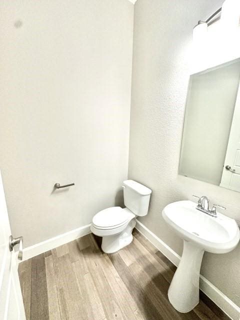 half bath featuring baseboards, toilet, and wood finished floors