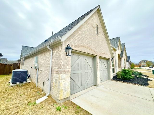 view of home's exterior with brick siding, roof with shingles, central air condition unit, concrete driveway, and an attached garage