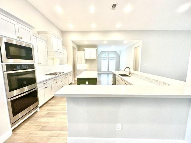 kitchen with visible vents, light countertops, appliances with stainless steel finishes, white cabinetry, and a peninsula