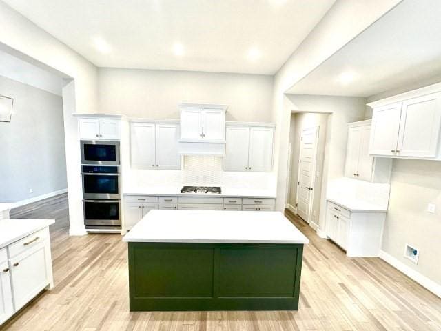 kitchen featuring white cabinetry, light countertops, appliances with stainless steel finishes, light wood-type flooring, and a center island