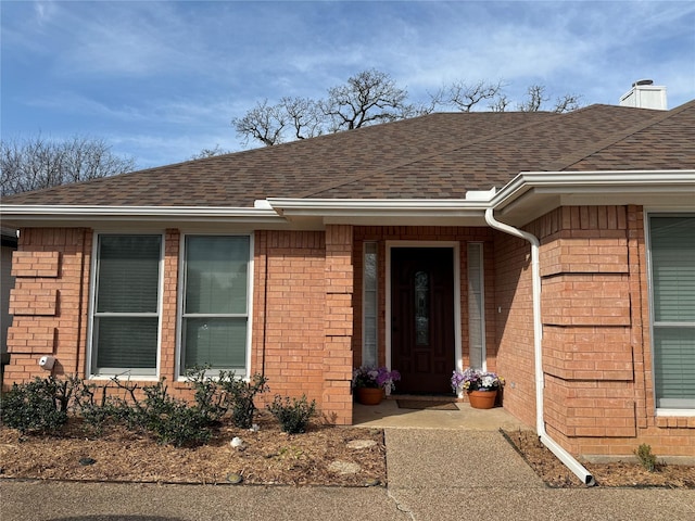 property entrance with brick siding, a chimney, and roof with shingles