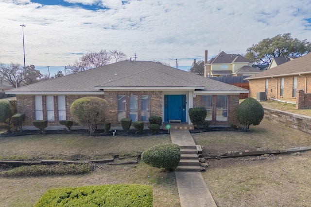 bungalow-style home featuring a front lawn, a shingled roof, brick siding, and central air condition unit