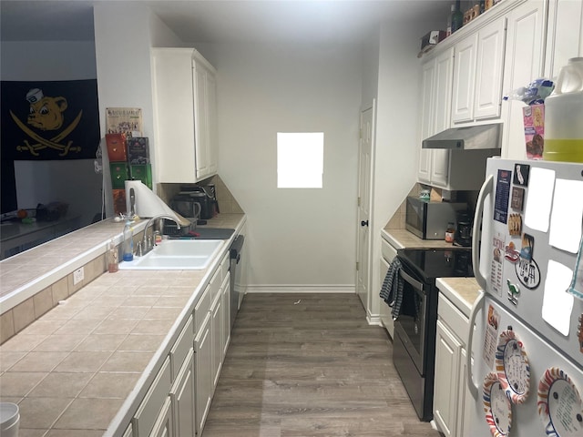 kitchen with tile counters, white cabinets, stainless steel appliances, under cabinet range hood, and a sink