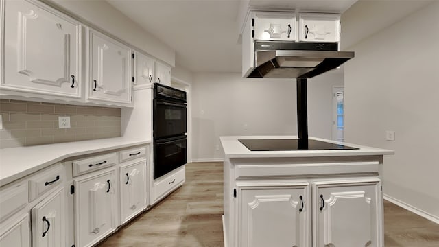 kitchen featuring tasteful backsplash, light countertops, white cabinetry, under cabinet range hood, and black appliances