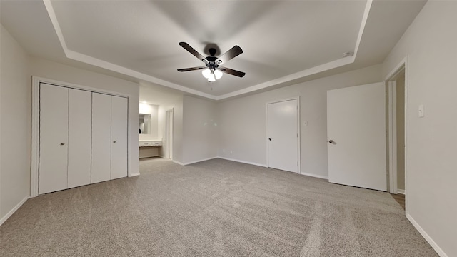 unfurnished bedroom featuring a tray ceiling, a ceiling fan, light carpet, connected bathroom, and baseboards