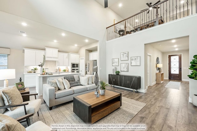 living room featuring recessed lighting, visible vents, a high ceiling, light wood-type flooring, and baseboards