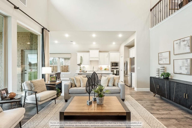 living room featuring light wood-style flooring, recessed lighting, a high ceiling, visible vents, and baseboards