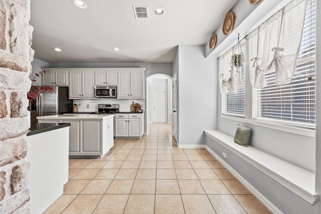 kitchen featuring arched walkways, light tile patterned floors, a kitchen island, visible vents, and appliances with stainless steel finishes