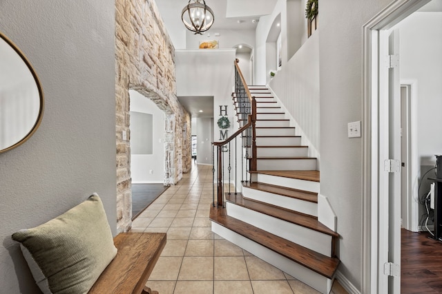 entryway featuring light tile patterned floors, a high ceiling, baseboards, stairs, and an inviting chandelier