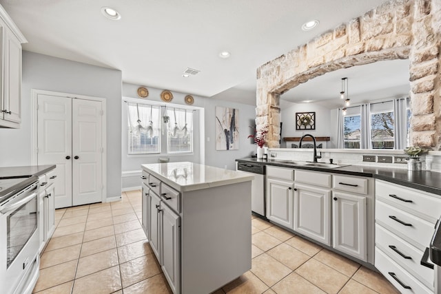 kitchen with stainless steel appliances, a kitchen island, a sink, hanging light fixtures, and dark countertops