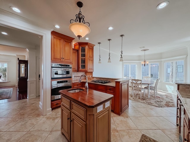 kitchen with glass insert cabinets, a sink, brown cabinetry, a center island with sink, and pendant lighting