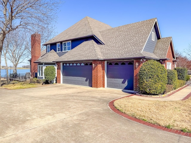 view of front of property with driveway, a garage, roof with shingles, a water view, and brick siding