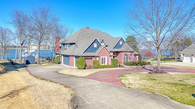 view of front facade with a garage, brick siding, a water view, driveway, and a front yard