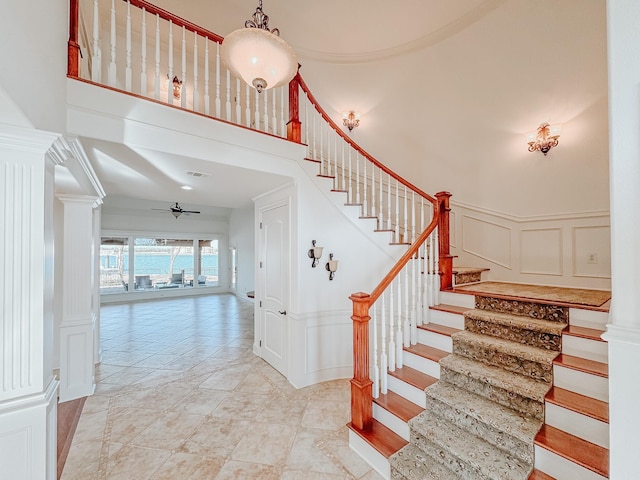 stairway with ceiling fan, a high ceiling, visible vents, and a decorative wall