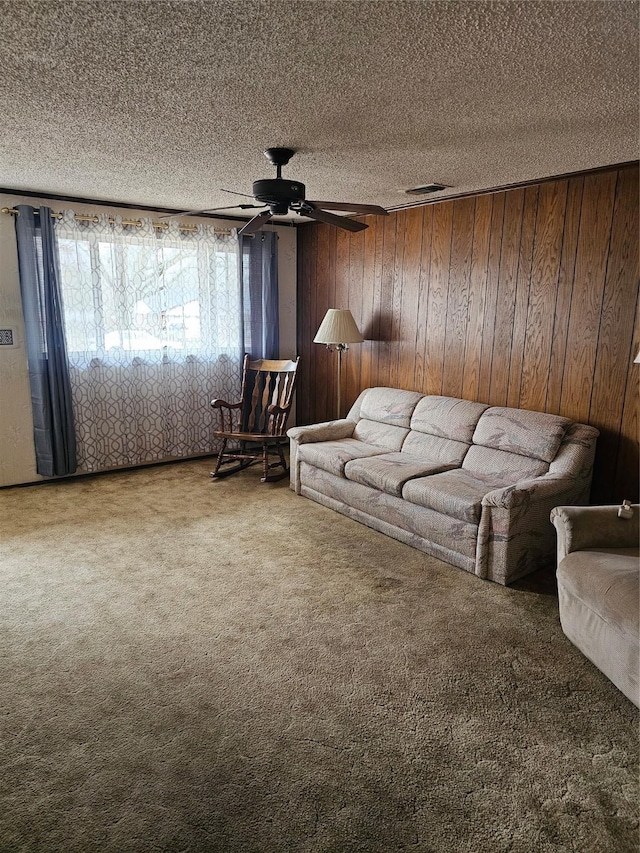 unfurnished living room with carpet floors, visible vents, a ceiling fan, a textured ceiling, and wooden walls