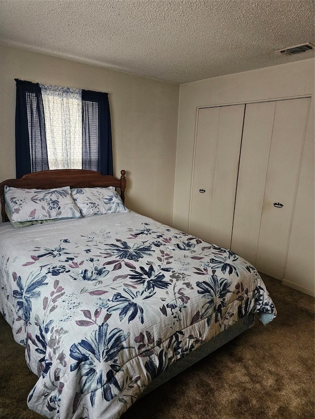 bedroom with a textured ceiling, visible vents, dark colored carpet, and a closet