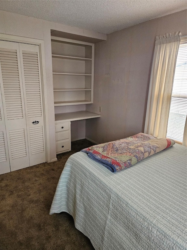 bedroom with a textured ceiling, built in desk, a closet, and dark carpet