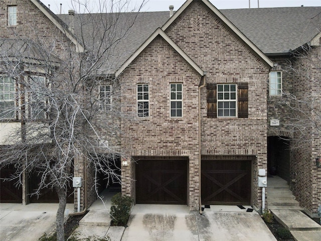 view of front facade with a garage, driveway, brick siding, and roof with shingles