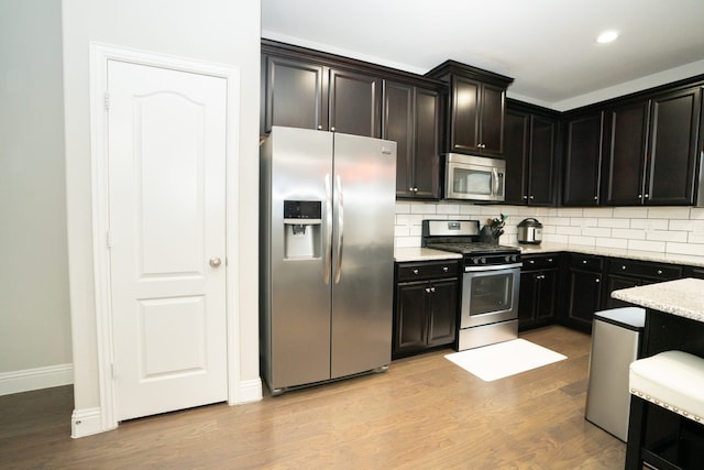 kitchen with light wood-type flooring, light stone countertops, stainless steel appliances, and decorative backsplash