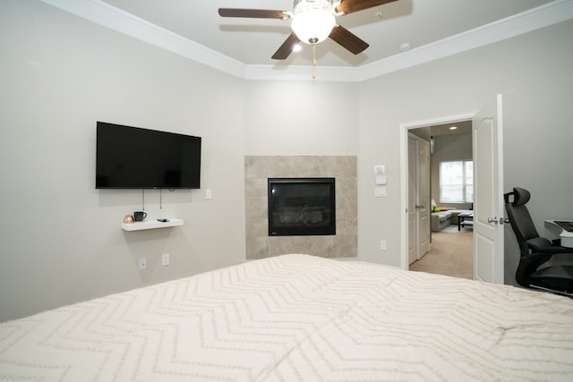 bedroom featuring light carpet, a tiled fireplace, a ceiling fan, and crown molding