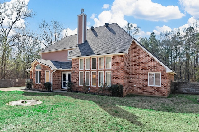 back of property with brick siding, a shingled roof, fence, a lawn, and a chimney