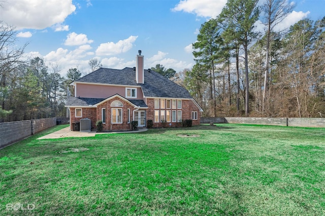 back of property with a fenced backyard, a yard, roof with shingles, brick siding, and a chimney