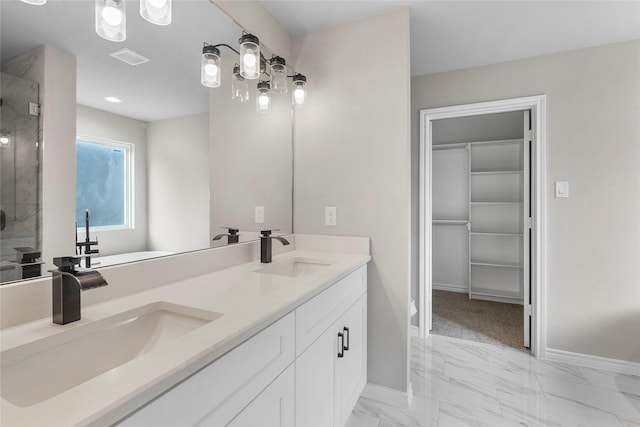 bathroom featuring marble finish floor, a shower stall, a walk in closet, and a sink