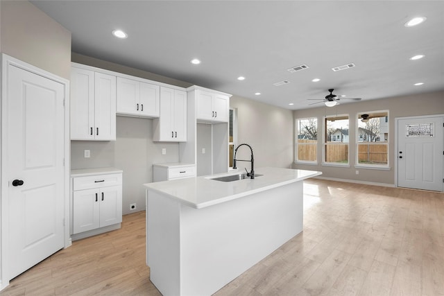 kitchen featuring light wood-style floors, white cabinetry, visible vents, and a sink