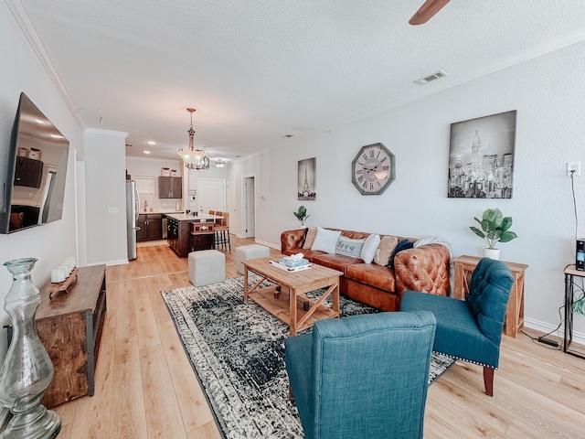 living room with crown molding, visible vents, light wood-style flooring, a textured ceiling, and baseboards