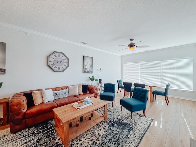 living area with crown molding, visible vents, a ceiling fan, a textured ceiling, and light wood-type flooring