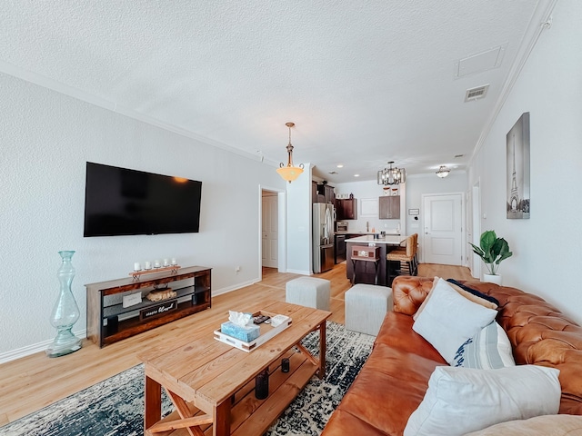 living room featuring a textured ceiling, light wood finished floors, visible vents, and crown molding