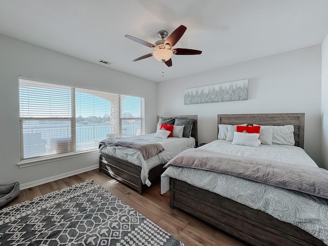 bedroom featuring a water view, wood finished floors, visible vents, and a ceiling fan