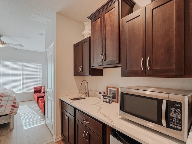 kitchen with stainless steel microwave, a sink, dark brown cabinetry, and light stone countertops