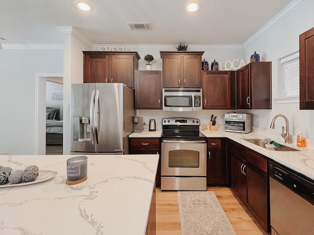 kitchen featuring visible vents, appliances with stainless steel finishes, light wood-style floors, ornamental molding, and a sink