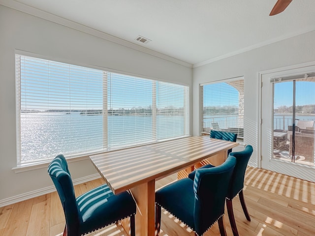 dining room with a water view, visible vents, ornamental molding, wood finished floors, and baseboards