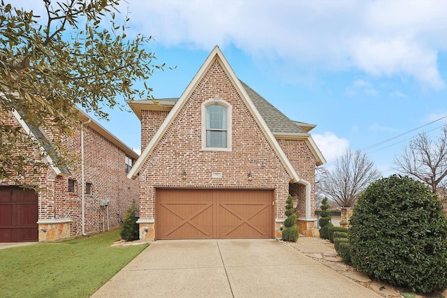 english style home featuring an attached garage, roof with shingles, concrete driveway, and brick siding