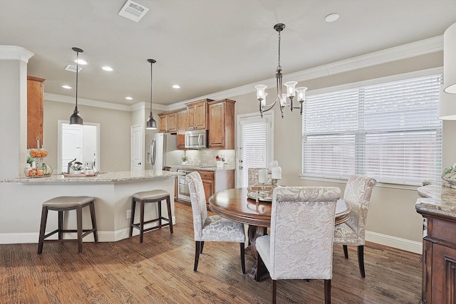 dining space with a notable chandelier, wood finished floors, visible vents, baseboards, and crown molding