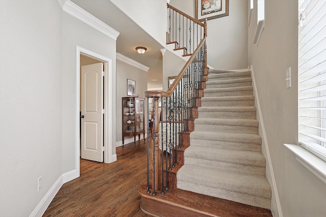 stairs featuring ornamental molding, wood finished floors, a towering ceiling, and baseboards