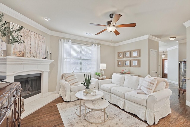 living room featuring a fireplace with raised hearth, ornamental molding, wood finished floors, and visible vents