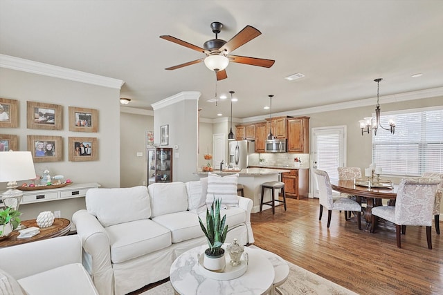 living area with recessed lighting, ceiling fan with notable chandelier, visible vents, ornamental molding, and light wood finished floors