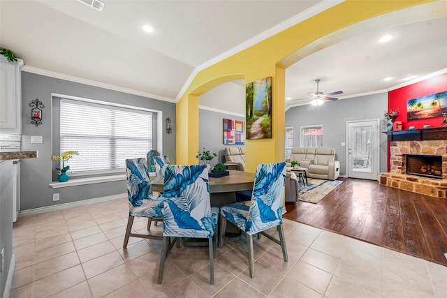 dining room featuring arched walkways, crown molding, light tile patterned flooring, a stone fireplace, and baseboards