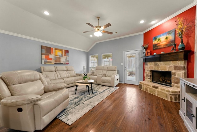 living area with dark wood-style floors, lofted ceiling, ornamental molding, ceiling fan, and a stone fireplace