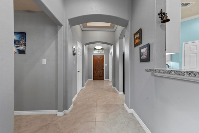 hall featuring baseboards, visible vents, arched walkways, and light tile patterned flooring