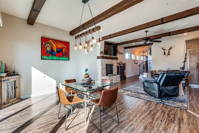 dining space featuring baseboards, beamed ceiling, wood finished floors, stairs, and a stone fireplace