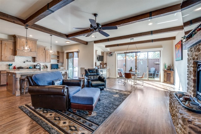 living area featuring a stone fireplace, a ceiling fan, baseboards, light wood-style floors, and beam ceiling